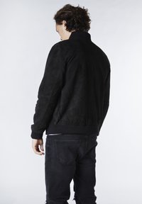 Svart mockajacka i bomberstil med ribbat krage och muddar. Har en texturerad yta och en solid design, bärs med mörka jeans.