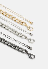 Fem metal kæder i guld, sølv og sort, med forskellige link-stilarter og lobster-låse. Glat tekstur med shiny finish.