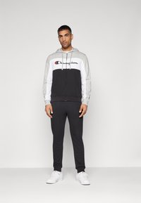 Hoodie med dragkedja i grått, svart och vitt med en logotyp, matchad med svarta joggers och vita sneakers. Slät textur, atletisk passform.