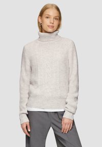Jasnoszary sweter dziany z wysokim golfem, z teksturowanym wzorem prążkowym i detalami o splocie warkoczowym, w zestawieniu z szarymi spodniami.