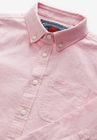 Camicia button-down rosa realizzata in cotone. Presenta un colletto, quattro bottoni, una tasca a toppa e un logo ricamato sulla tasca.