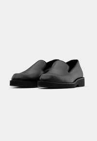 Sorte slip-on sko lavet af glat læder med rund tå og en lav, solid sort sål. Minimalistisk design uden synligt hardware.