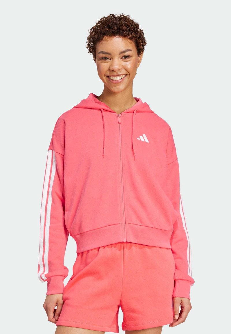 Rosa zip-up hettegenser laget av mykt materiale, med hvite tre-striper på ermene og en kort design. Kombinert med matchende shorts.