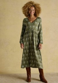 Zelené šaty s kvetinovým vzorom, dlhé, s výstrihom do V a zŕastveným pásom, doplnené hnedými cowboyskými booti s detailným prešívaním.