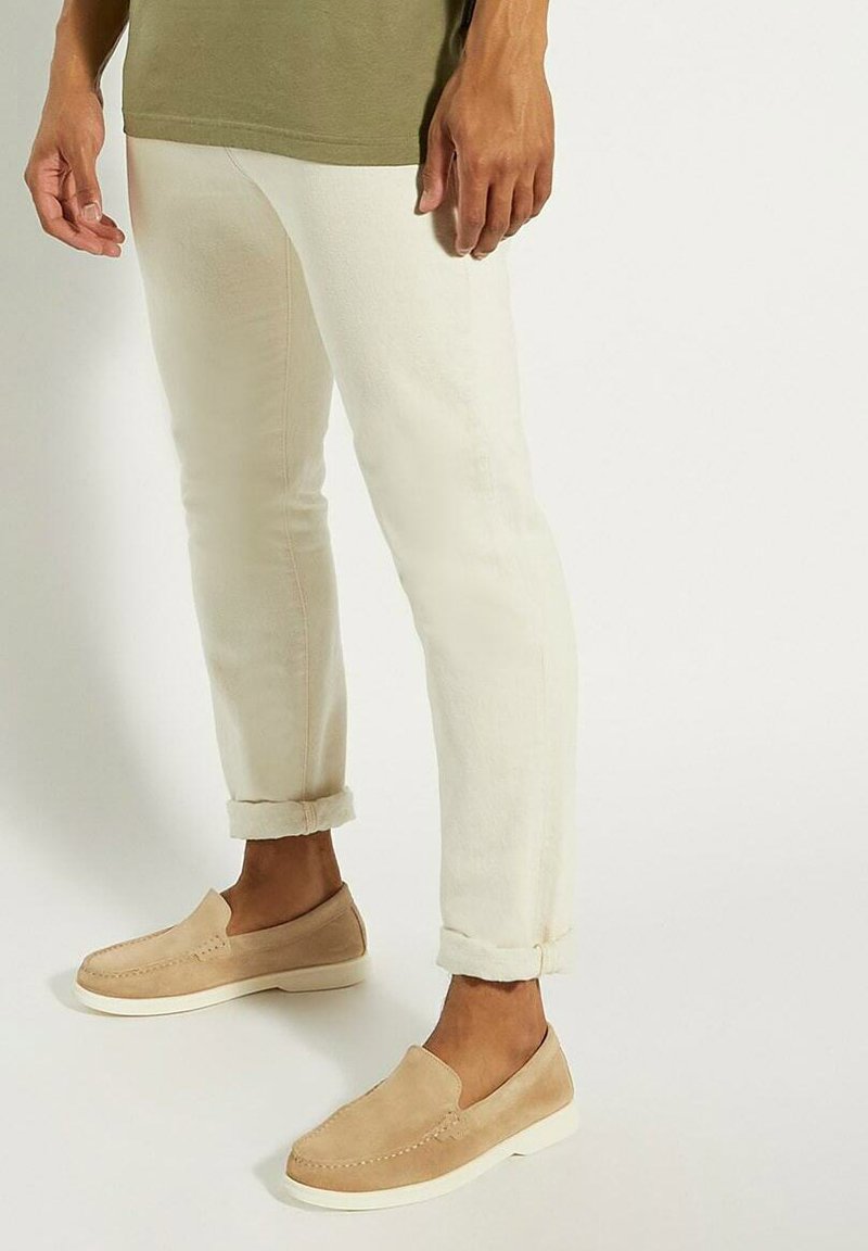 Beige suède instap schoenen met een witte zool, gecombineerd met opgerolde crème-kleurige broeken en een olijfgroen T-shirt.
