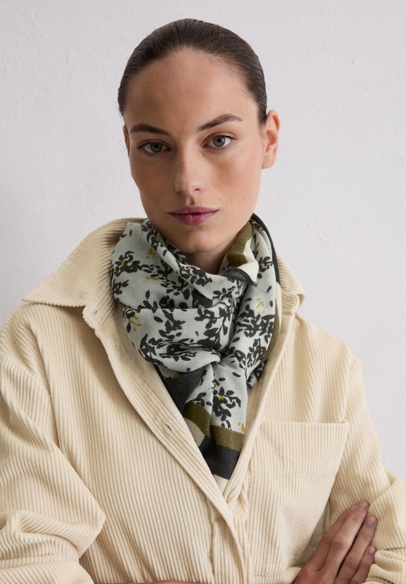 Blumenmuster-Schal in Mintgrün, Schwarz und Oliv, um den Hals gewickelt. Weiche Textur mit einem gemütlichen, oversized Design.