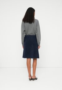 Námořnická modrá áčková sukně s texturovaným, nadýchaným povrchem. Kombinována se šedým topem s dlouhým rukávem. Nosit s černými vysokými podpatky.