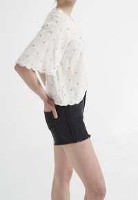 White short-sleeve blouse with gold dot pattern, scalloped edges, paired with black denim shorts featuring a frayed hem and side pockets.