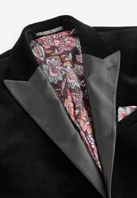 Blazer de terciopelo negro con solapas de satén, que presenta un forro con un colorido patrón floral. Incluye un detalle a juego en el pañuelo de bolsillo con el mismo patrón.