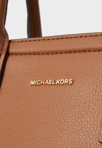 Sac à main en cuir marron avec une surface texturée et un logo doré "MICHAEL KORS". Présente des lignes épurées et des coutures robustes.