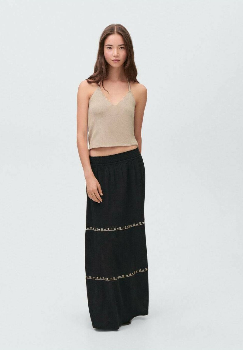 Beige cropped tank top with thin straps paired with a long black skirt featuring decorative gold stitching and an elastic waistband.