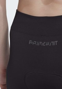 Leggings noirs taille haute avec une texture lisse. Présentent un logo gris sur la ceinture et des coutures renforcées à l'arrière.