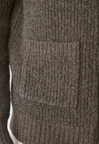 Brauner gerippter Strickcardigan mit einer Vordertasche. Die Textur ist weich und kuschelig, mit einem Reißverschluss an der Seite.