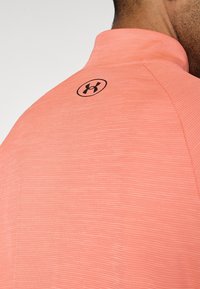 Κοντομάνικο αθλητικό πουκάμισο κοραλλί με υφασμάτινη υφή. Διαθέτει ψηλό γιακά και κυκλικό μαύρο λογότυπο στο πίσω μέρος κοντά στον λαιμό.