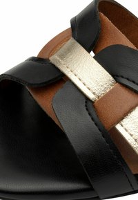 Černé kožené sandály s zlatým kovovým páskem a hnědými koženými akcenty. Design zahrnuje široký, otevřený tvar se šitými detaily.