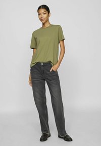 Olivgrön kortärmad t-shirt i kombination med löst sittande svarta jeans. T-shirten har en rund halsringning; jeansen har en slitna fåll och framfickor.