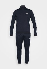 Survêtement Adidas bleu marine avec veste à fermeture éclair complète, logos de marque sur la poitrine, la manche et le pantalon, poignets élastiques et pantalons fuselés.