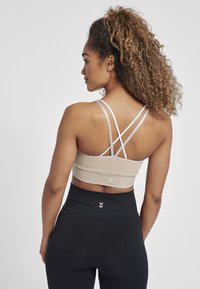 Beige sportbh med korsade axelband, texturerad nedre del och logodetalj. Kombinerad med högmidjade svarta leggings.