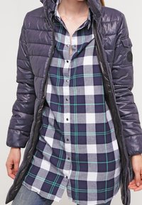 Purple puffer jacket with a hood, featuring a glossy texture, layered over a navy, white, and green plaid button-up shirt.
