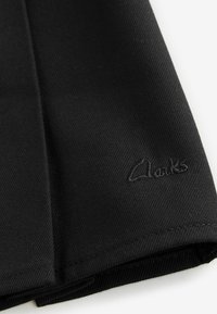 Tissu noir avec une finition texturée, présentant un logo "Clarks" brodé dans le coin inférieur droit. Design simple et plat.