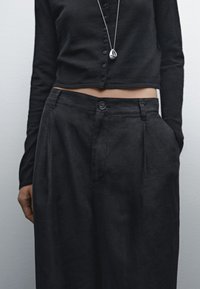 Svart knappad långärmad topp som kombineras med högmidjade svarta byxor. Byxorna har framfickor och en enda knappstängning.