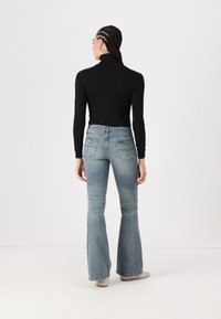 Svart langermet topp og lyseblå vide jeans. Jeansene har et lappemerke på baklommen og en falmet vask. Jeansen har en jevn tekstur.