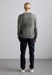 Grå stickad tröja med långa ärmar, rund halsringning och en avslappnad passform, kombinerad med mörkblå jeans och vita sneakers.