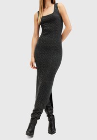 Femme portant une robe midi sans manches en maille torsadée gris foncé avec une fente latérale, associée à des bottes noires souples montantes jusqu'aux genoux.