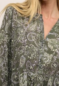 Groene blouse met paisleyprint, knoopsluiting, V-hals en zachte stof. Bevat ingewikkelde bloem- en spiraalontwerpen voor extra detail.