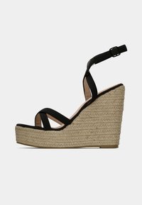 Black wedge sandals feature an espadrille-style jute sole, a closed heel with an adjustable strap, and crisscross straps across the front.