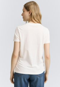 T-shirt blanc à manches courtes en coton doux avec un col rond. Présente une coupe décontractée, une texture lisse et un design simple.