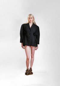 Čierny oversize blejzer s textúrovaným povrchom, ktorý má veľké gombíky a detaily v podobe pom-pom. Doplní ho jeden pár jedinečných čižiem s rozstrapkaným lemom.