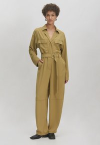 Beiger Jumpsuit mit Kragen, vorderen Taschen und tailliertem Bund. Verfügt über lange Ärmel und weite, gerade Beine. Glatte Stoffoberfläche.