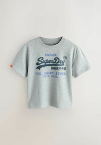 Šedé bavlněné tričko s krátkými rukávy, na kterém je námořnicky modrý vintage nápis „SuperDry“ a oranžová etiketa na rukávu.
