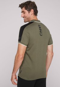 Olivgrünes Polohemd mit schwarzen Schulterakzenten, weißer Paspelierung an den Ärmeln und Logodetail auf der Rückseite, gefertigt aus weichem, atmungsaktivem Stoff.