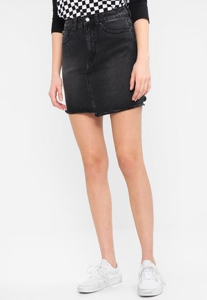Mini-jupe en denim noir avec un ourlet effiloché, cinq poches et passants de ceinture. Associée à un haut à carreaux et des baskets blanches.