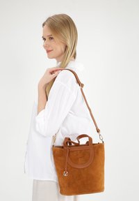 Bruine suède handtas met leren accenten, afgeronde bovenkant, dubbele handvatten en een afneembare schouderriem. Compact en gestructureerd ontwerp.