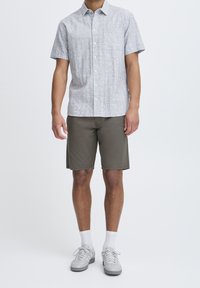 Short-sleeve button-up shirt in light gray with a textured pattern, paired with olive green shorts, white socks, and gray sneakers.