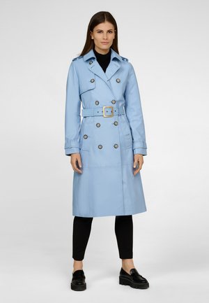 Manteau trench bleu clair avec un design à double boutonnage, de grands boutons, une ceinture ajustable à la taille et des épaulettes. Stylé avec un pantalon et des chaussures noirs.