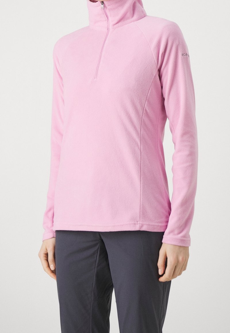 Ljust rosa fleecetröja med halvdragkedja, långa ärmar och en figurnära passform, matchad med mörka byxor för kontrast.