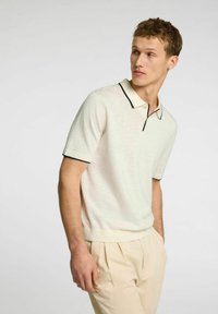 Polo shirt beige chiaro realizzato in tessuto morbido, con un bordo a contrasto di blu scuro sul colletto e sulle maniche, con una silhouette aderente.