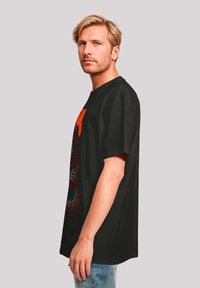 Black cotton t-shirt featuring a colorful graphic design, short sleeves, and a relaxed fit. Notable colors include red and blue accents.