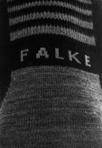 Sorte og grå mønstrede sokker med vandrette striber nær toppen, med mærket "FALKE" strikket i hvid. Blød tekstur.