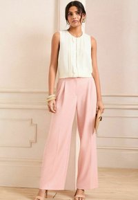 Cream sleeveless top with a textured front, paired with light pink wide-leg trousers. Accessories include a bracelet and clutch.