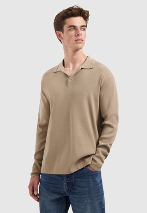 Beige lange mouwen polo shirt gemaakt van een gestructureerde stof met een kraag en een knoopsluiting met twee knopen, gecombineerd met blauwe jeans. Eenvoudig en casual ontwerp.