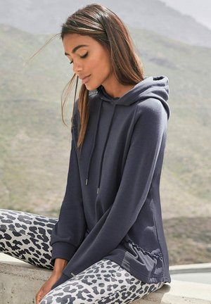 Marineblauer Hoodie mit Kordeln, weichem Textil und seitlichen Details, kombiniert mit grauen Leggings mit schwarzem Leopardenmuster.