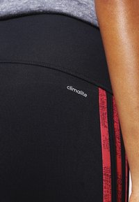 Collant sportivi neri con una texture liscia, dotati di una striscia laterale a motivo rosso e di un piccolo logo "climalite" sulla vita.