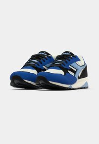Μπλε και μαύρα αθλητικά παπούτσια με υφή στην επιφάνεια, διαθέτουν λευκή ενδιάμεση σόλα και μαύρη εξωτερική σόλα από καουτσούκ. Πολύ-στρωματικός σχεδιασμός με κορδόνια.