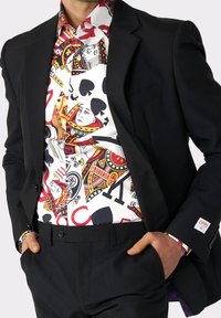 Veste de costume noire par-dessus une chemise colorée présentant des motifs de cartes à jouer, principalement en rouge, noir et blanc, avec des motifs complexes.