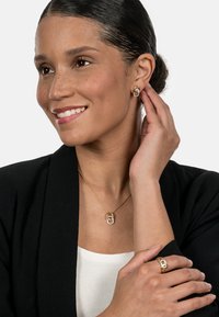 Gold jewelry featuring a pendant necklace with a chain, a ring with intertwined design, and hoop earrings adorned with stones.